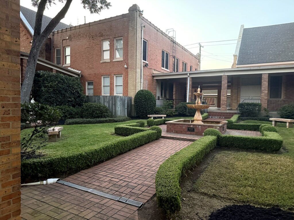 Formal brick courtyard with a stone fountain, clipped boxwood hedging and a paver walkway