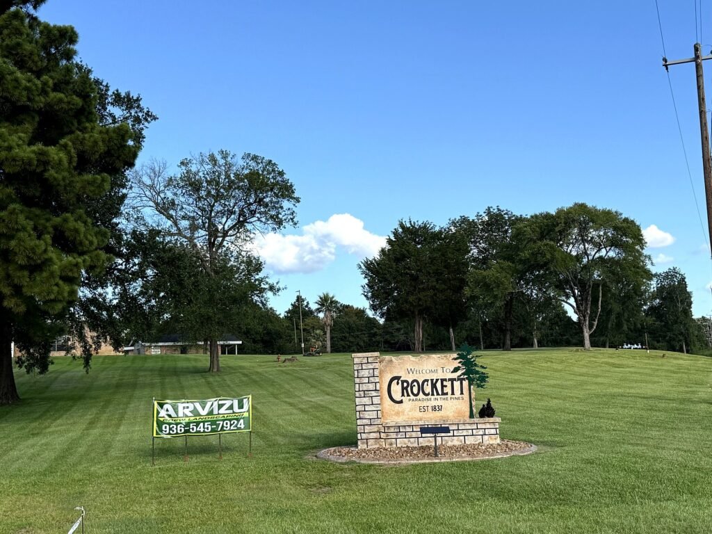 Arvizu Crew Landscaping banner beside the Welcome to Crockett sign on a striped public lawn