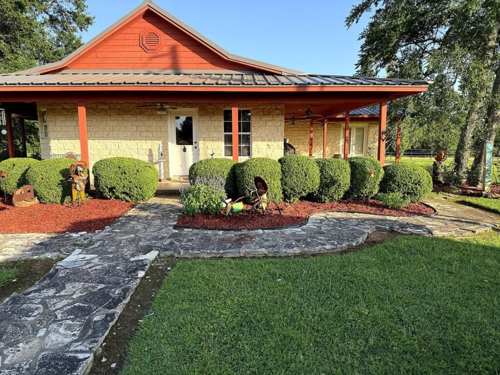 Stone home with rounded shaped hedges, red mulch beds and a flagstone walkway