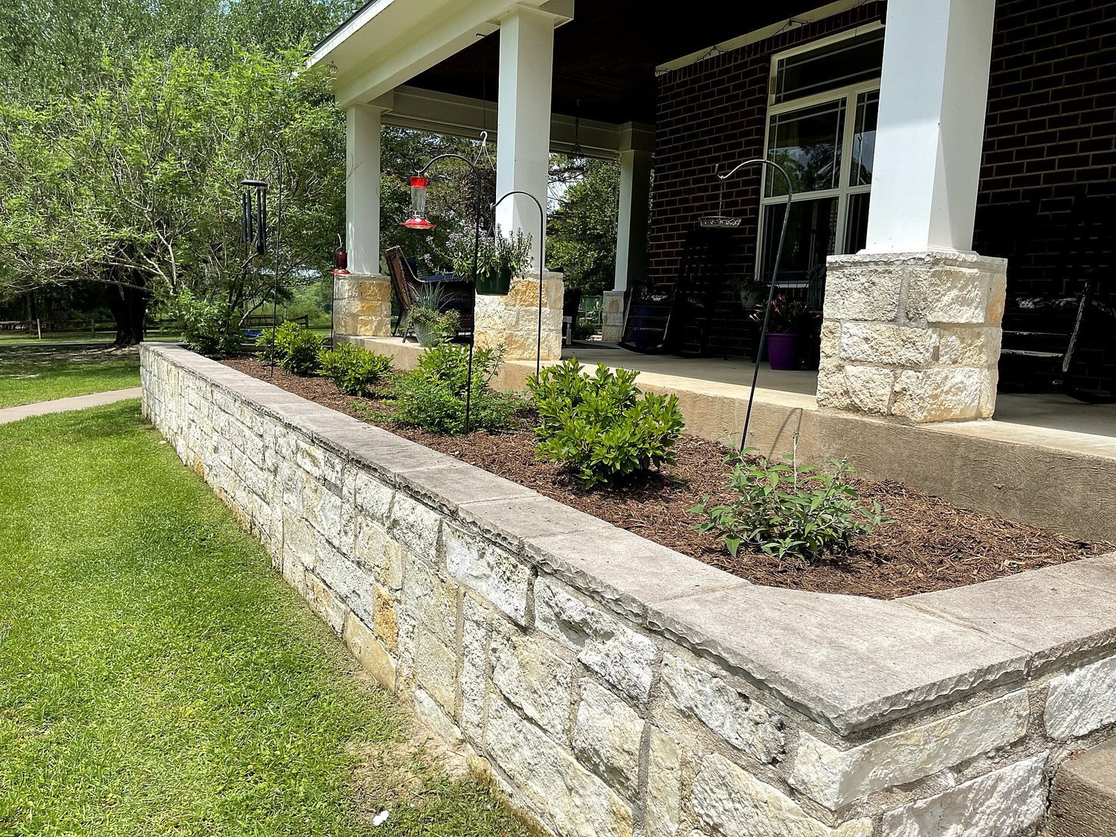 Stone retaining wall planter bed with fresh plantings along a covered porch