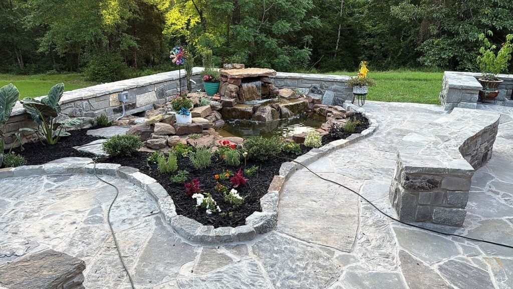 Flagstone patio with a stacked stone water feature, mulched beds and flowering plants